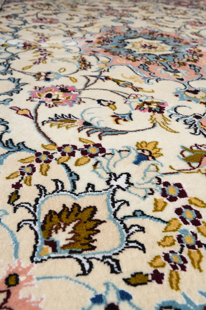 A close-up of an ornate patterned rug with a cream background and intricate floral motifs in light blue, pink, mustard yellow, and brown.