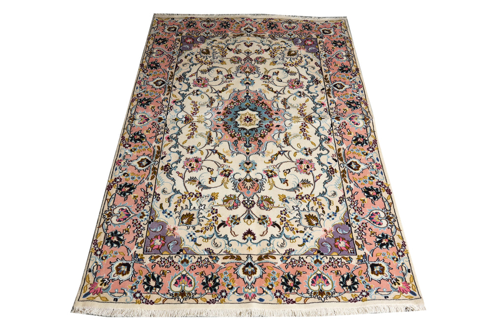 A rectangular traditional area rug with an intricate floral and medallion pattern, featuring a cream center, a dusty pink border, and multicolored accents including blue, green, and orange, shown against a plain white background.