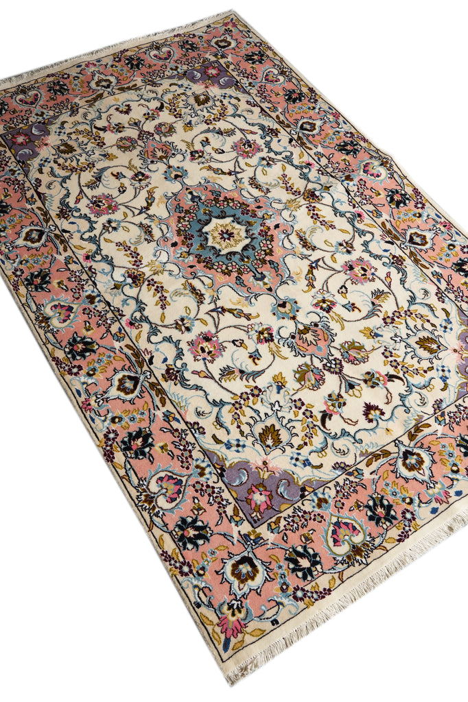 A traditional Persian-style area rug with an intricate floral pattern, featuring a cream center, a dusty pink border, and accents of blue, green, and gold, shown on a plain white background.