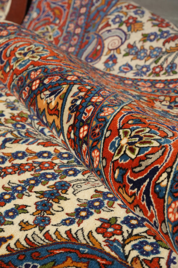 A close-up of a folded patterned rug showing detailed floral and ornamental motifs in red, blue, orange, and cream.