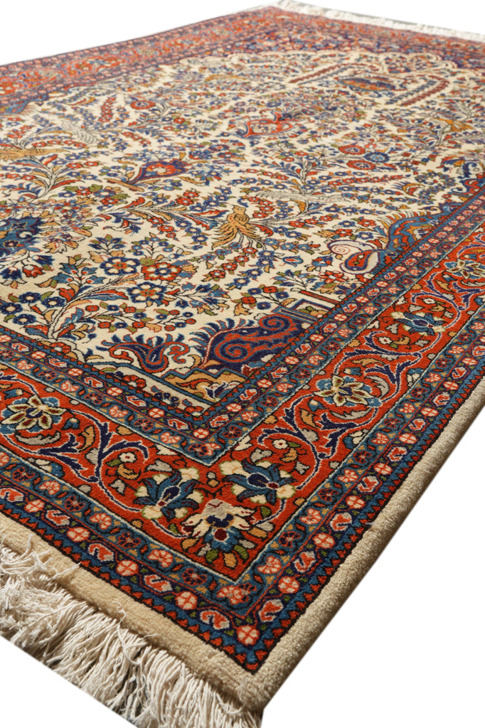 An ornate traditional Persian-style area rug with a cream background, featuring intricate red, blue, and orange floral and vine patterns, complete with a decorative border and cream fringe on one end.