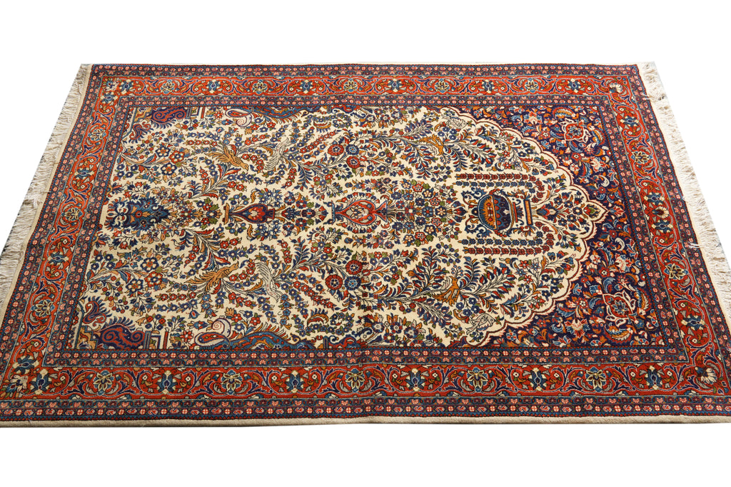 An ornate traditional Persian-style area rug with a complex floral and geometric pattern, featuring a cream center, deep red and navy borders, and cream fringe on the sides.