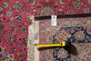 Load image into Gallery viewer, A close-up of a patterned area rug with a bright pink field, blue border, and cream fringe, shown with a tape measure and product tag to indicate size.