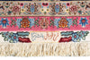 Load image into Gallery viewer, Close-up of an ornate patterned rug with cream fringe, featuring floral motifs in pink, blue, orange, and green, plus Arabic calligraphy on a rectangular central panel.