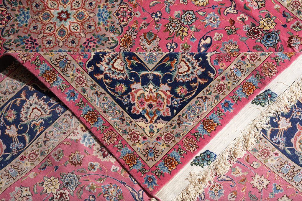 A close-up of a traditional oriental rug with a vibrant pink field, featuring a central navy blue and beige medallion, ornate floral borders, and cream-colored fringe.