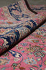 Load image into Gallery viewer, A close-up of a rolled area rug showing its intricate floral and paisley patterns in pink, navy blue, beige, and green.