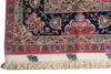 Load image into Gallery viewer, A close-up of a traditional oriental rug corner showing a dark navy blue field with ornate floral motifs, a pink border, beige inner bands, and cream fringe along the bottom edge.