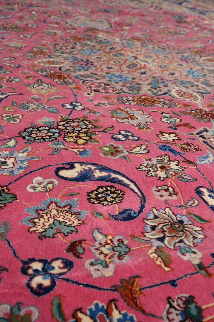 A close-up of a pink patterned rug with intricate floral and paisley motifs in blue, cream, green, and gold tones.