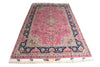Load image into Gallery viewer, A traditional oriental area rug with a pink field, navy blue borders, and intricate floral motifs in beige, green, and blue, finished with cream fringe on the ends.