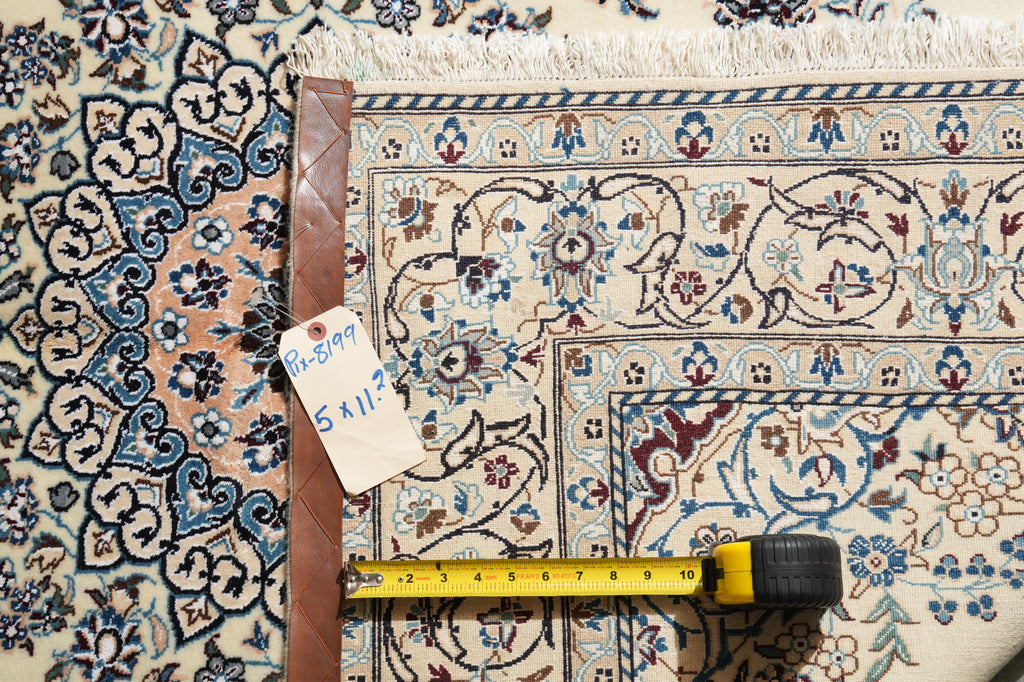 A patterned area rug with a cream, blue, and brown traditional design, shown with a tape measure and a handwritten tag on a wooden stand.