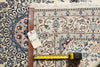 Load image into Gallery viewer, A patterned area rug with a cream, blue, and brown traditional design, shown with a tape measure and a handwritten tag on a wooden stand.