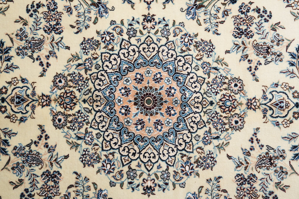 A close-up of an ornate floral patterned rug with a central medallion in cream, blue, and dusty pink tones.