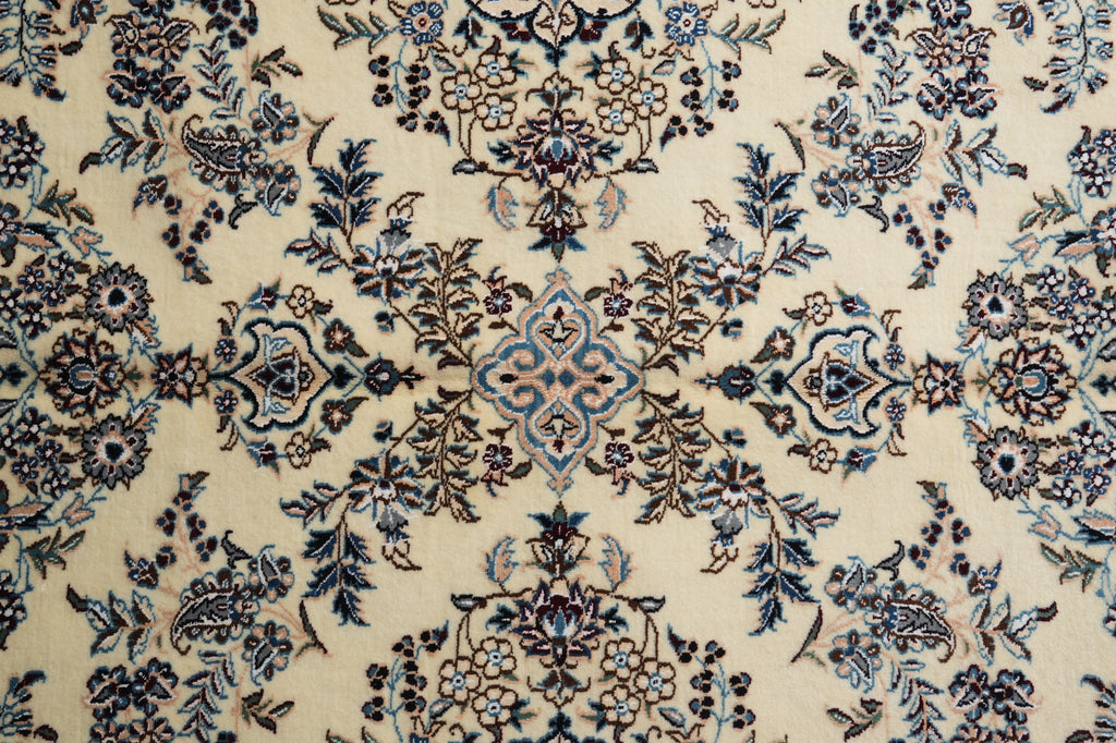 A close-up of an ornate floral patterned textile or rug with a cream background and detailed blue, brown, and muted gold motifs.