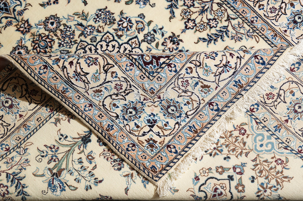 A close-up of a traditional Persian-style area rug with an intricate floral and vine pattern in blue, brown, and beige on a cream background.