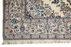 Load image into Gallery viewer, Close-up of an ornate area rug corner showing a cream base with intricate blue, brown, and beige floral and vine patterns and fringe along one edge.