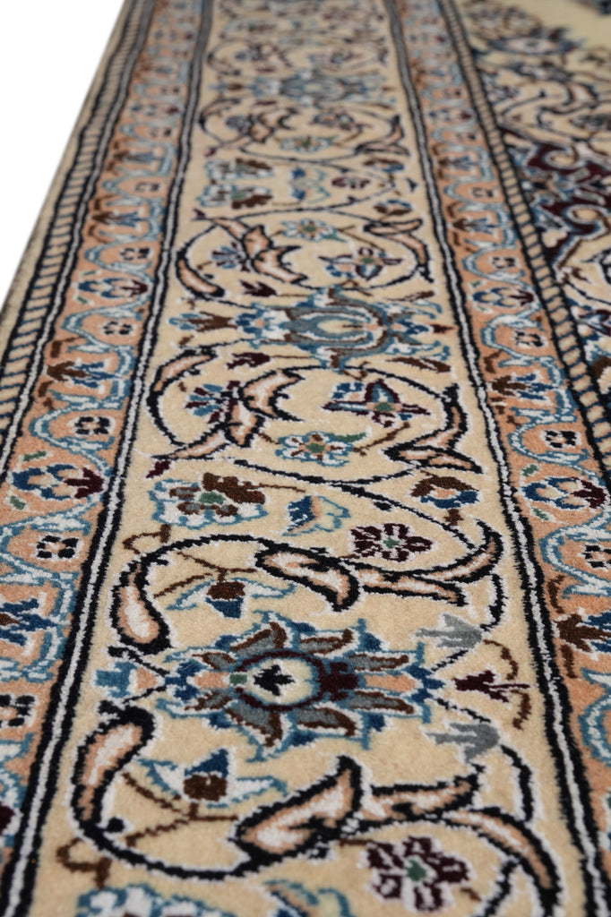 A close-up view of an ornate area rug with a traditional floral pattern in beige, blue, brown, and black.