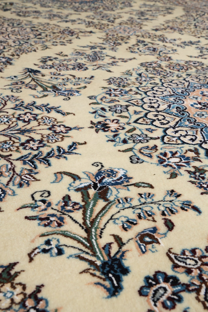 Close-up of an ornate floral patterned rug with cream background and blue, green, and brown embroidered motifs.