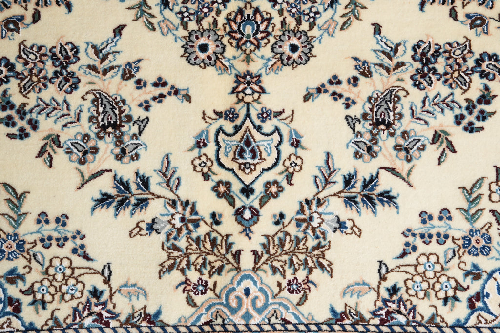 A close-up of an ornate traditional rug pattern with a cream background and detailed floral motifs in blue, brown, and black.