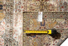 Load image into Gallery viewer, An ornate traditional patterned rug shown in a close-up flat lay, with a yellow tape measure laid across the center and a white product tag attached near the top. The rug has a cream base with red, blue, and brown floral and geometric motifs.