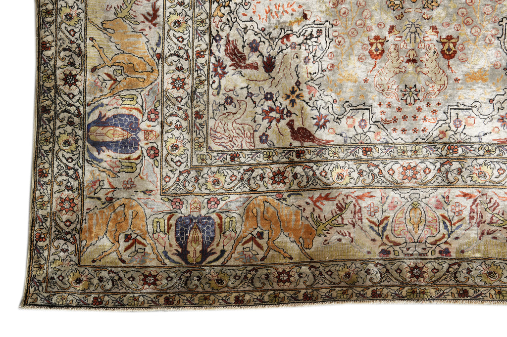 A close-up of an ornate vintage-style rug corner showing detailed floral and animal motifs in beige, brown, blue, and rust tones.