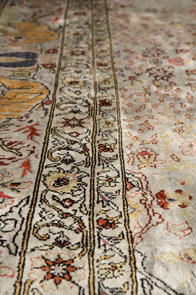 Close-up of an ornate patterned rug with cream, beige, red, blue, and yellow tones, showing detailed woven floral and geometric motifs.
