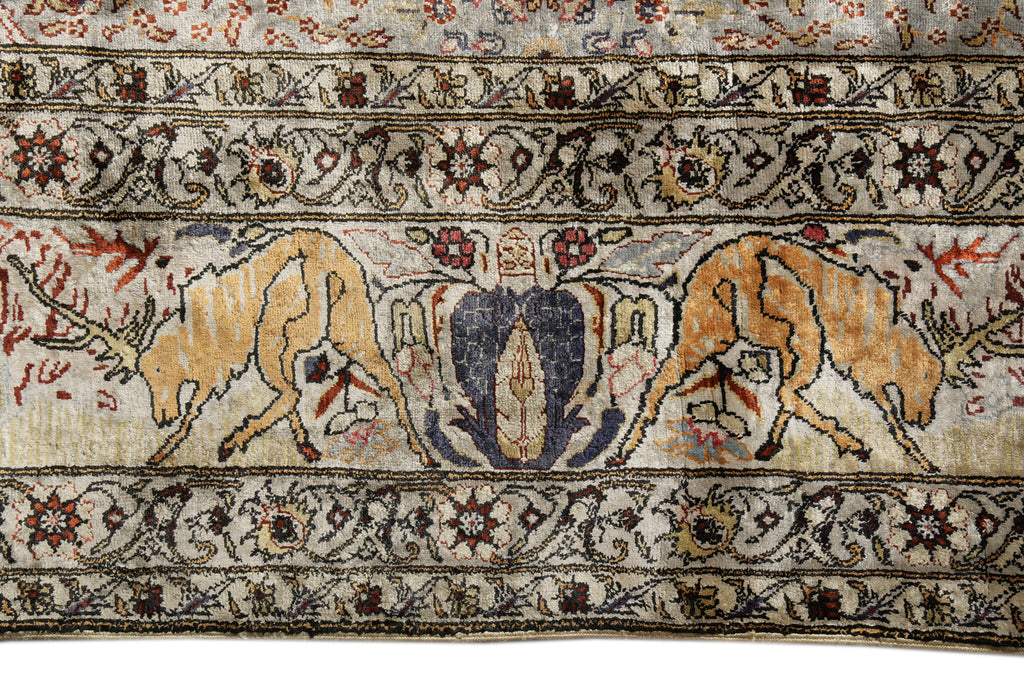 A close-up of an antique-style rug featuring two tan horses facing each other in a central field, flanked by ornate floral borders in beige, brown, navy, and red.