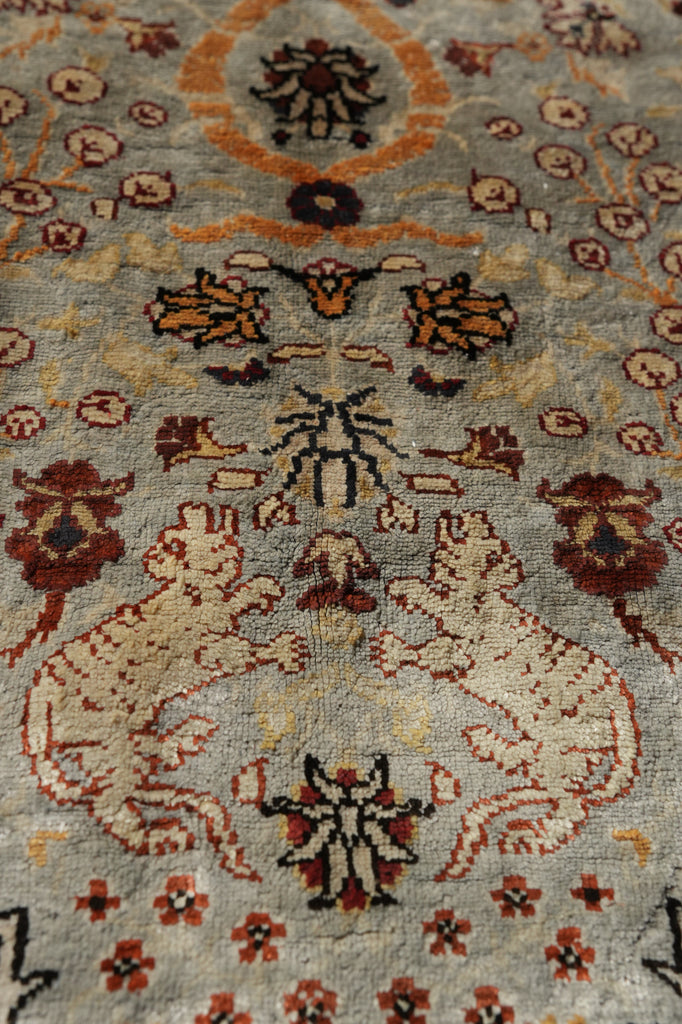 Close-up of an ornate patterned area rug with cream, rust, burgundy, and black motifs on a muted blue-gray field.