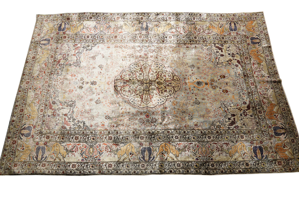 An antique Persian-style area rug with a faded beige and cream base, featuring a central medallion and ornate floral borders in muted brown, blue, and ochre tones.
