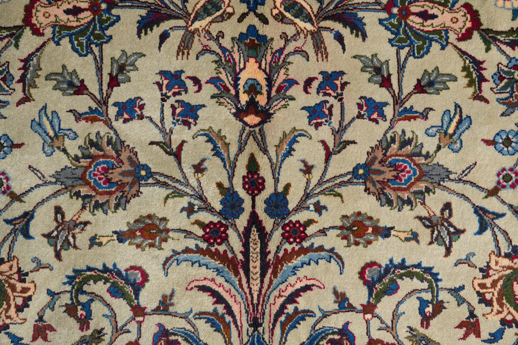 Close-up of an ornate floral patterned textile or rug with a cream background and detailed botanical motifs in blue, red, green, and brown.