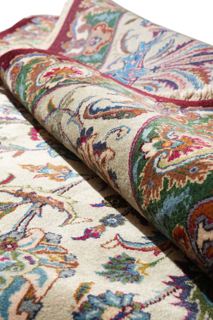 A close-up of a rolled area rug showing its detailed traditional pattern in cream, green, red, blue, and orange tones.