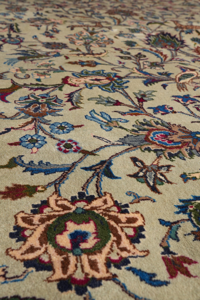Close-up of an ornate floral patterned rug with cream, blue, green, and rust tones on a beige background.