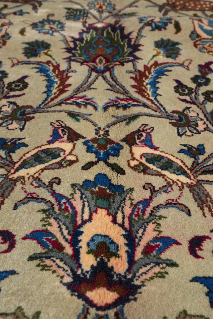 Close-up of a traditional patterned rug with a beige background and intricate floral and bird motifs in blue, red, green, and cream.