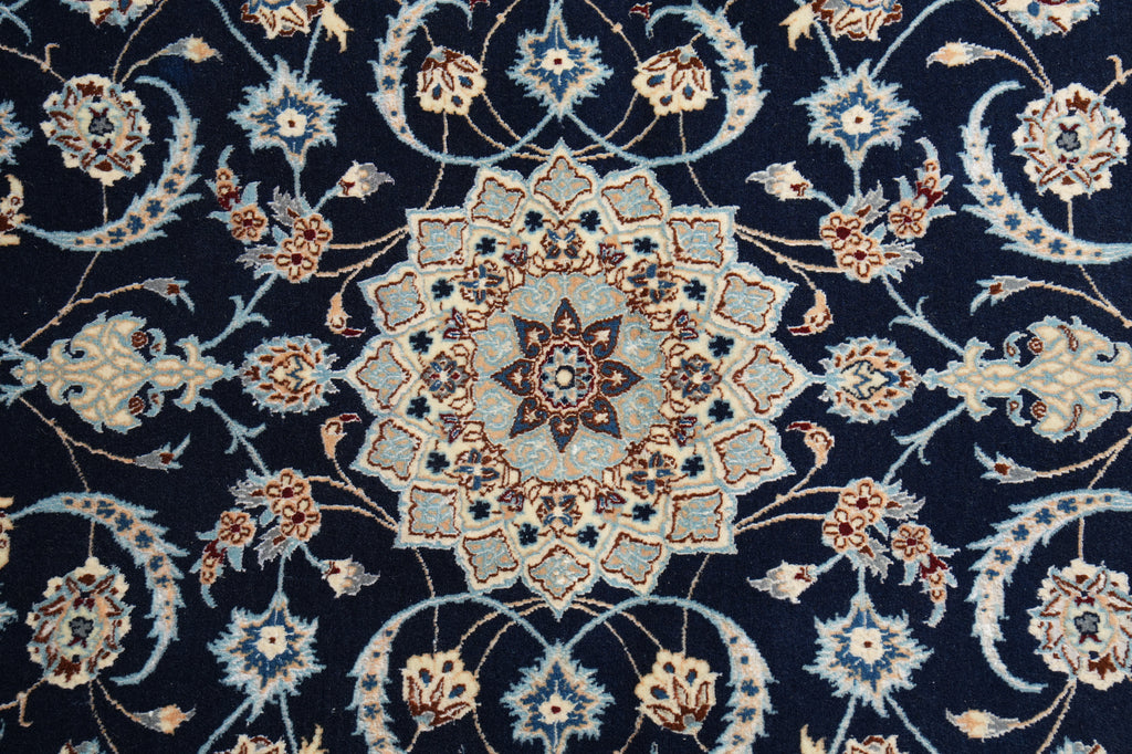 A close-up of an ornate traditional rug featuring a central medallion and scrolling floral motifs in navy blue, beige, light blue, and rust brown.
