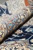 Load image into Gallery viewer, A close-up of a rolled area rug showing an intricate traditional pattern with navy blue, cream, light blue, and brown tones.