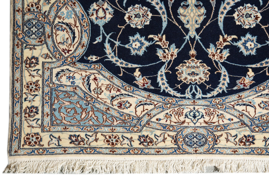 Close-up of an ornate area rug corner showing a dark navy field, cream border, and intricate floral motifs in blue, beige, and rust red with white fringe.