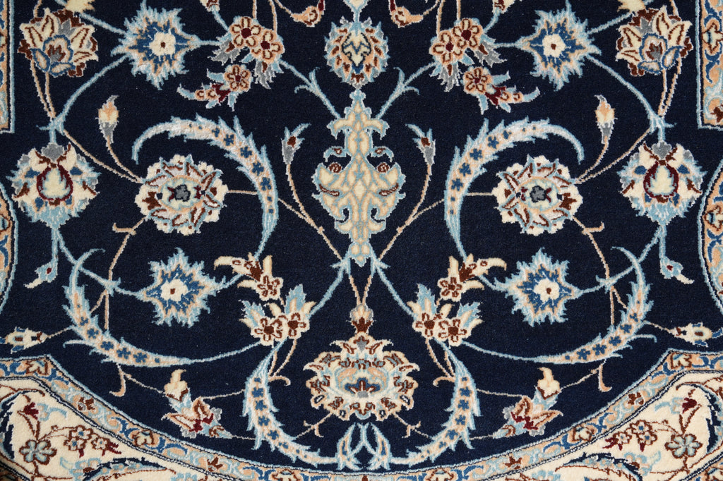 Close-up of an ornate traditional rug pattern with a dark navy blue field, cream and beige floral motifs, and light blue scrolling vine details.