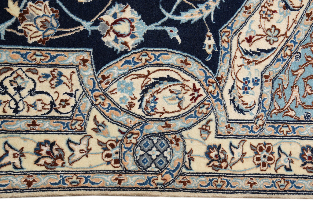 Close-up of a patterned area rug showing a navy blue field, cream borders, and intricate floral motifs in blue, brown, and beige.