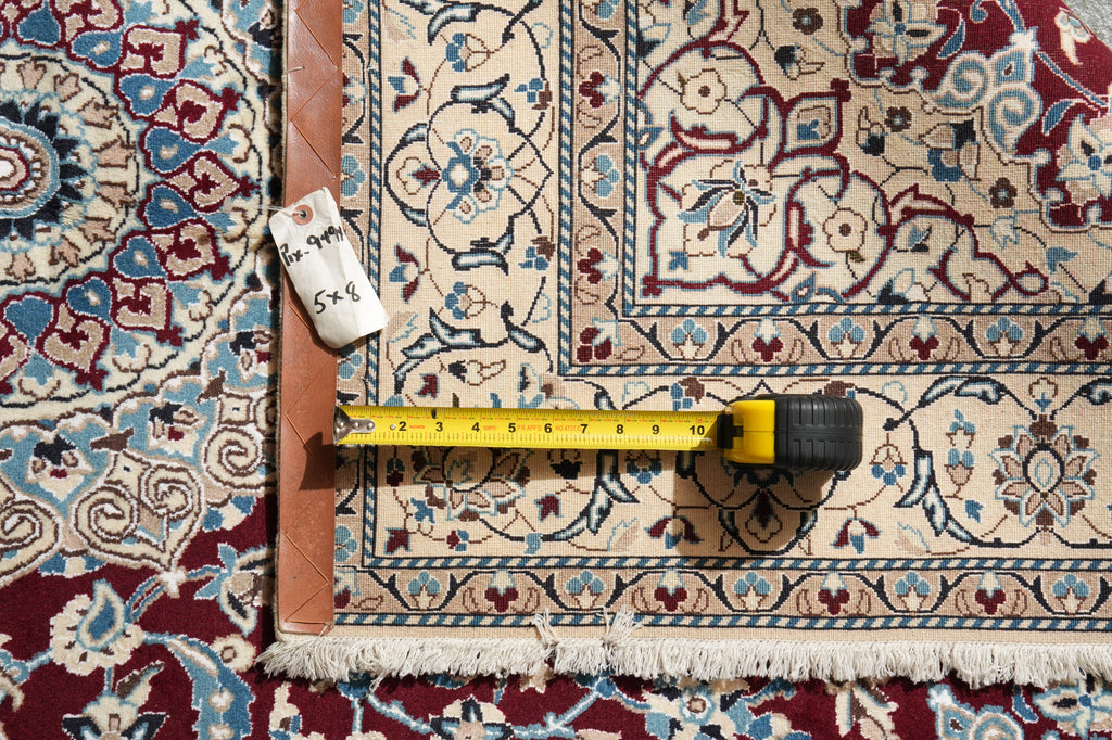 A close-up of a patterned area rug with a tape measure and a small handwritten tag placed on it to show dimensions.