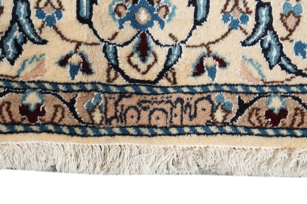 Close-up of a traditional patterned rug showing a cream base with blue, beige, and brown floral motifs and a fringed edge.