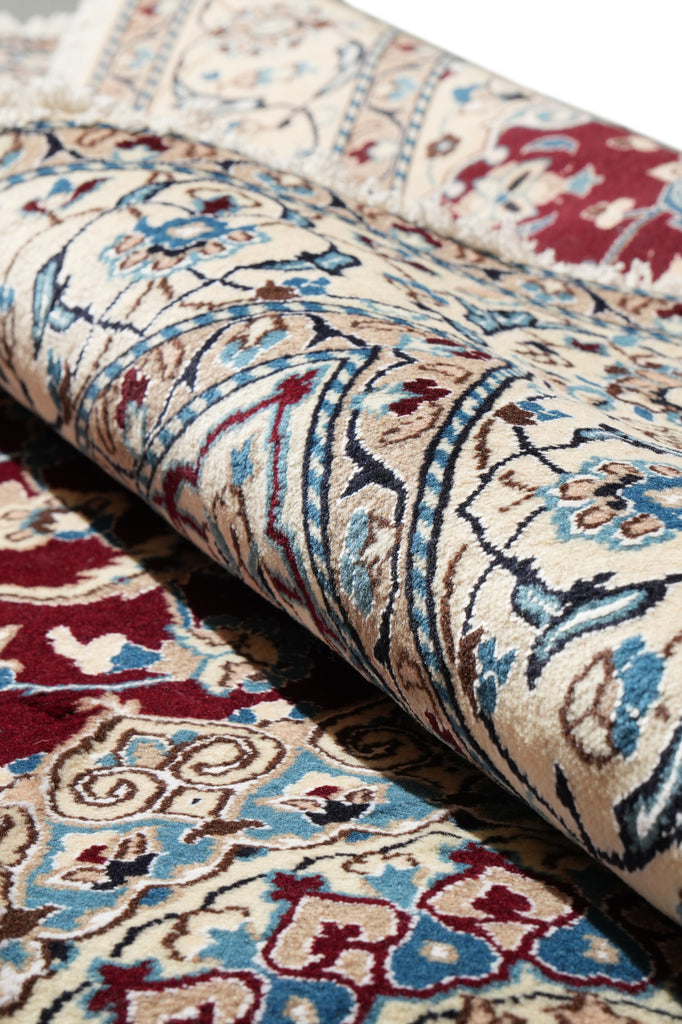 A close-up of a rolled area rug showing an intricate traditional pattern in beige, blue, red, and brown tones.