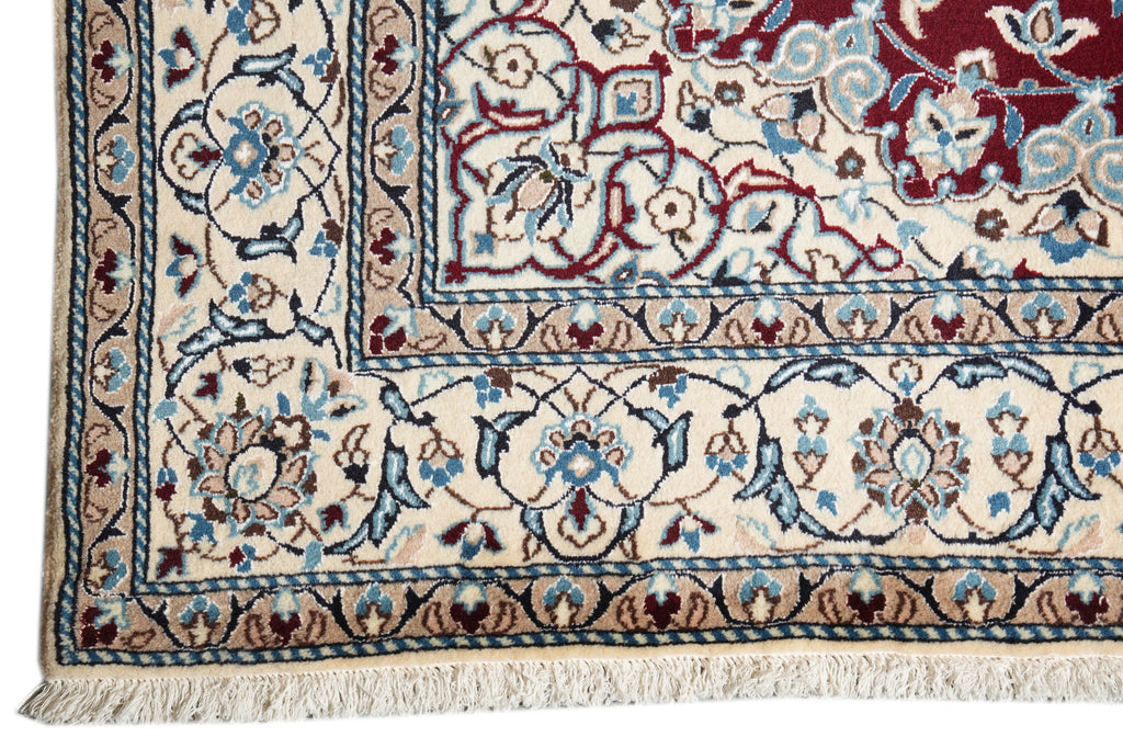 Close-up of an ornate patterned rug corner showing cream, burgundy, blue, and brown floral motifs with a fringed edge.