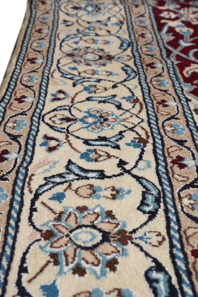 A close-up of a traditional patterned area rug with a cream base, featuring blue, brown, and red floral motifs and detailed borders.