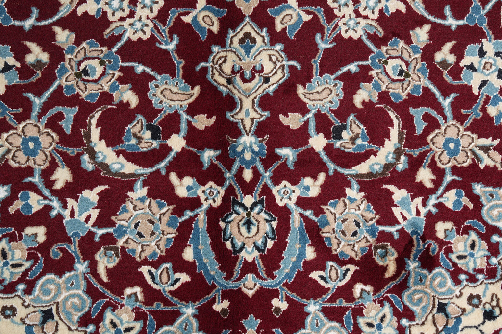 A close-up of an ornate patterned rug or textile with a deep burgundy background and cream and light blue floral and vine motifs.