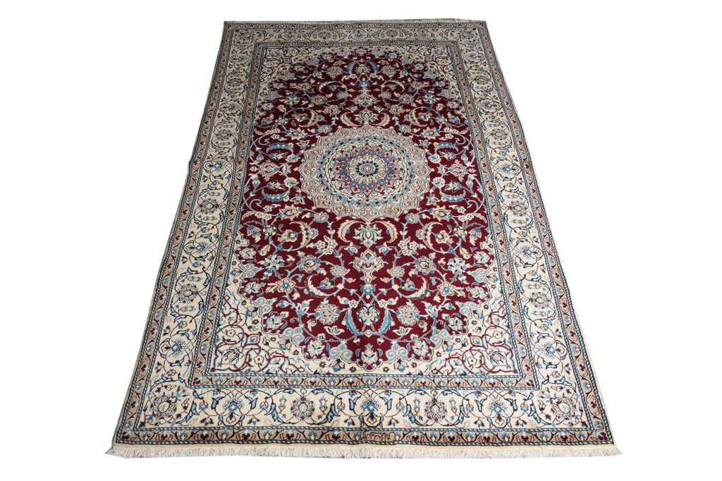 A traditional oriental area rug with a central medallion, featuring a deep red field, cream and beige borders, and blue accents, shown flat against a white background.