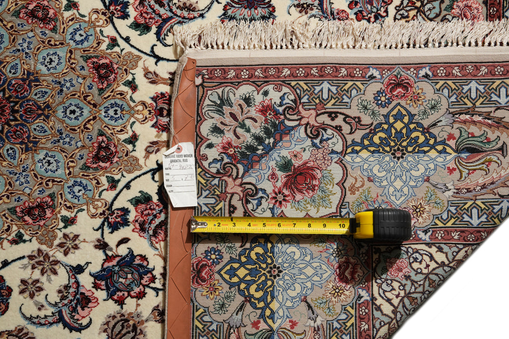 An ornate patterned area rug with cream, blue, red, and brown floral motifs, shown with a yellow tape measure and a small product tag laid across it to indicate scale.