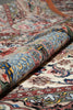 Load image into Gallery viewer, A close-up of a rolled area rug showing its detailed traditional pattern in cream, blue, red, yellow, and black.