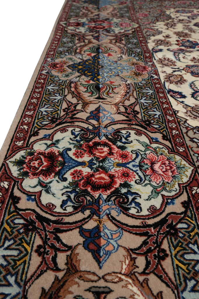 A close-up view of an ornate traditional area rug with a cream base, featuring a central floral medallion in red, pink, and blue, surrounded by detailed borders.