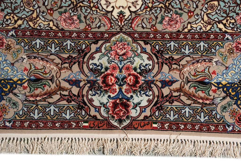 A close-up of an ornate Persian-style rug with a central floral medallion, intricate scrollwork, and cream fringe along the bottom edge.