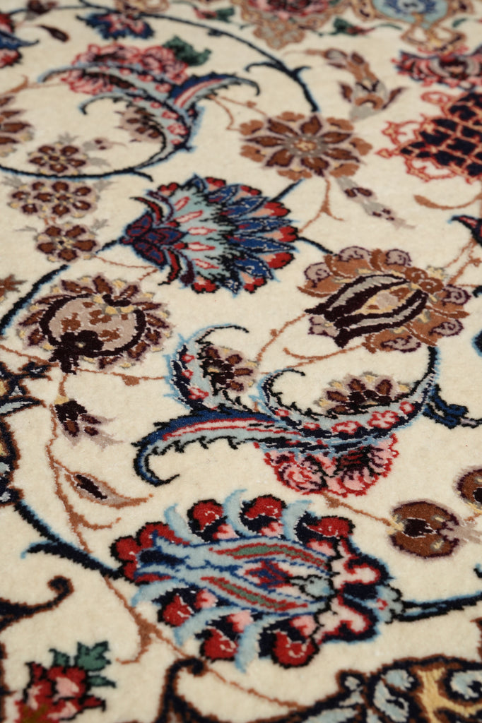 A close-up of an ornate floral and paisley patterned rug or textile on a cream background, with red, blue, brown, and black motifs.