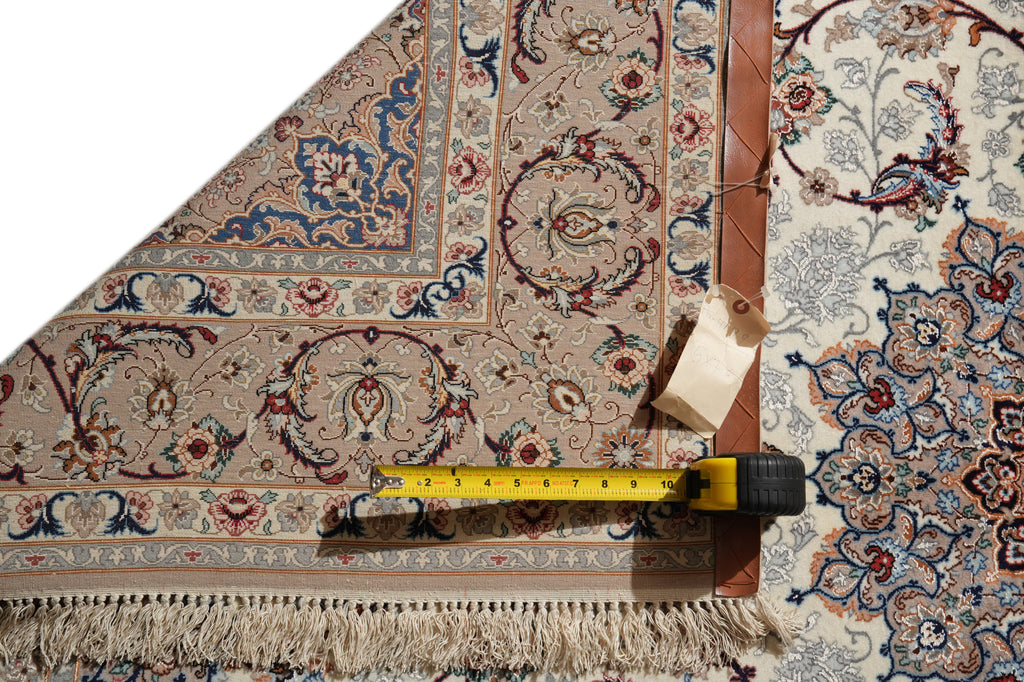 An ornate patterned area rug shown folded to display its design and fringed edge, with a yellow tape measure and paper tag placed along the bottom edge for scale.